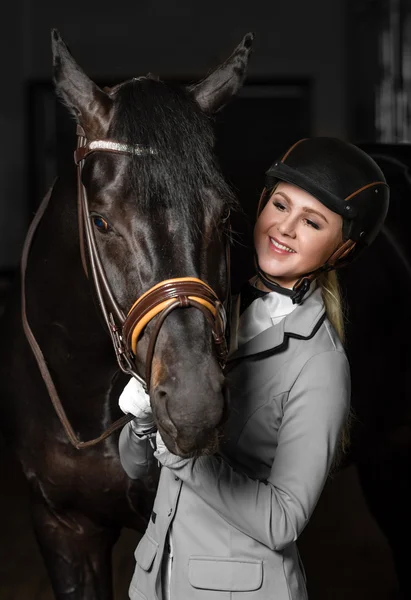 Jezdkyně v uniformě s hnědé koně ve stáji. — Stock fotografie