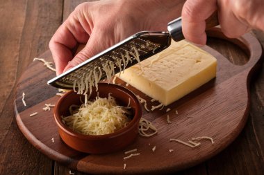 Kadın rendeleyiciye peynir sürüyor. Yakın plan..