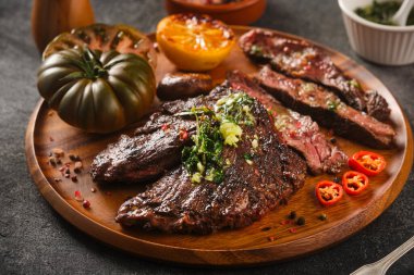 Hanger steak bbq with souce chimichurri on wooden plate, close up.