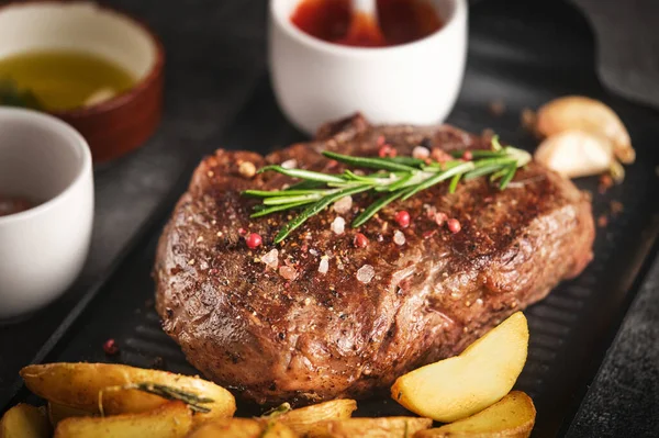 Juisy new york strip steak with rosemary, garlic and potato on skillet pan, close up, selective focus