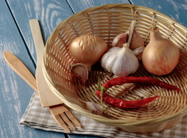 Basket with onions, garlic and red pepper on a wooden table — Stock Photo, Image