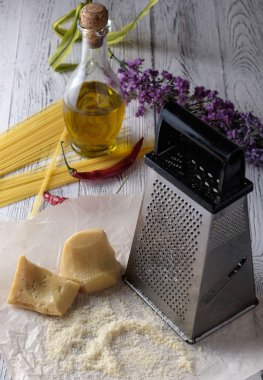 Rendelenmiş parmesan peyniri, şişe zeytinyağı ve üzerinde metal rende 