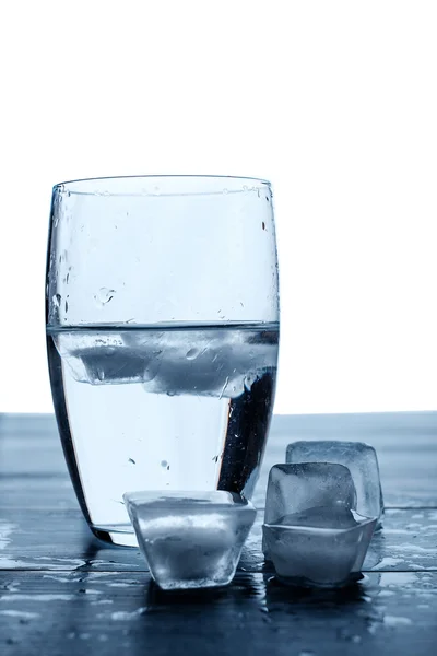 Стакан воды и тающие кубики льда на деревянном столе . — стоковое фото
