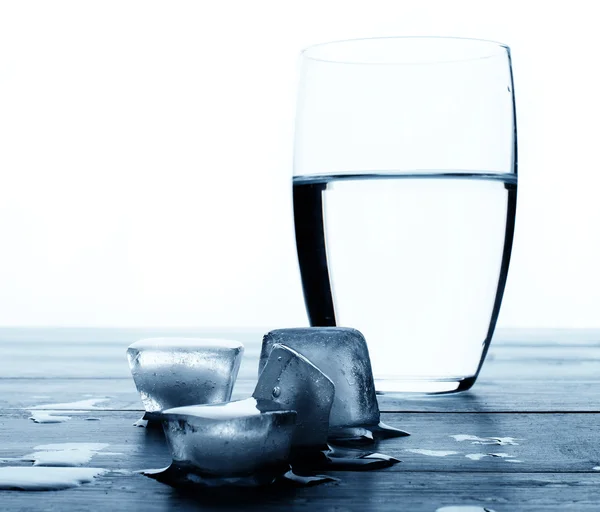 Glass of water and melting ice cubes on a wooden table. — Stock Photo, Image