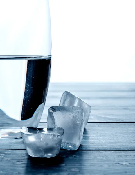 Bicchiere d'acqua e cubetti di ghiaccio fondenti su un tavolo di legno . — Foto Stock