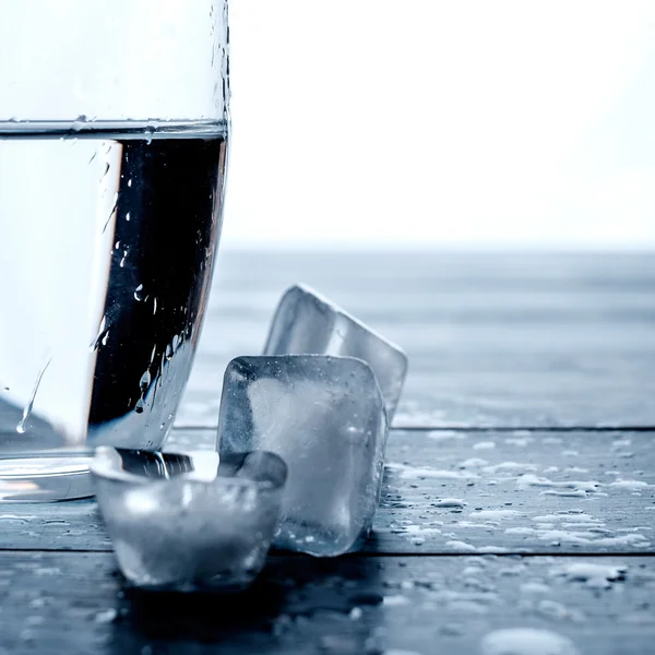 Glass of water and melting ice cubes on a wooden table. — Stock Photo, Image