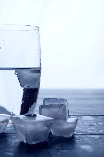 Bicchiere d'acqua e cubetti di ghiaccio fondenti su un tavolo di legno . — Foto Stock