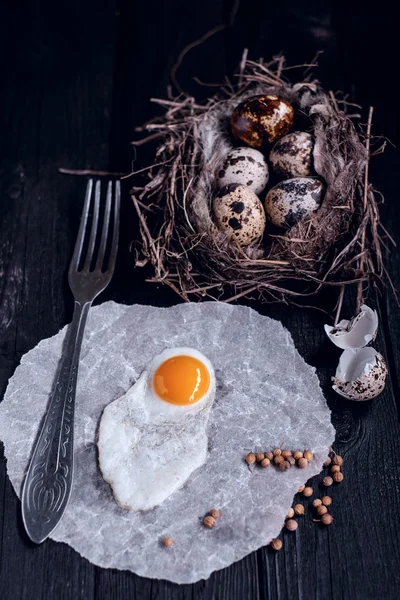 Quail eggs in the nest and a fried egg on a wooden board. — Stock Photo, Image