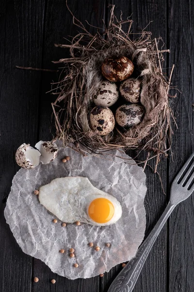 Ovos de codorna no ninho e um ovo frito em uma tábua de madeira . — Fotografia de Stock
