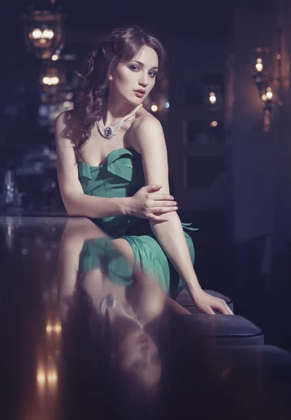 Elegante ragazza in abito verde seduta al bar — Foto Stock