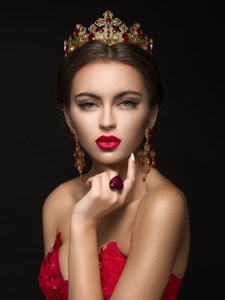 Beautiful girl in a golden crown and earrings on a dark backgrou — Stock Photo, Image