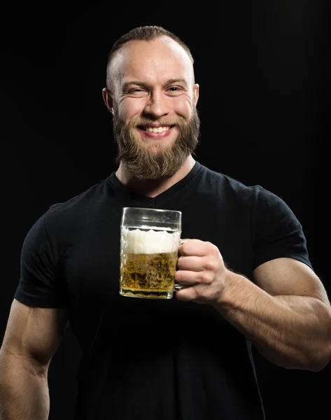 Sonriente hombre barbudo bebiendo cerveza de una taza de cerveza sobre bac negro —  Fotos de Stock