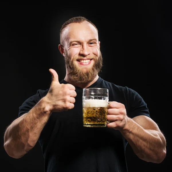 Homem barbudo bebendo cerveja de uma caneca de cerveja sobre fundo preto . — Fotografia de Stock