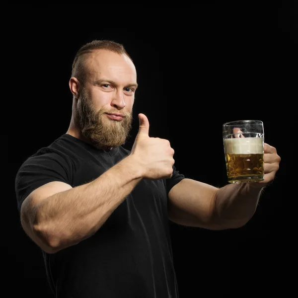 Uomo barbuto bere birra da una tazza di birra su sfondo nero . — Foto Stock
