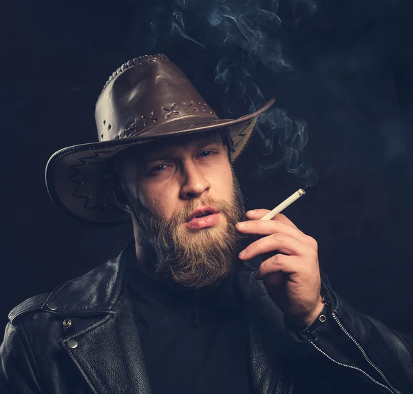 Homem fumador com barba e bigode usando um chapéu de cowboy . — Fotografia de Stock
