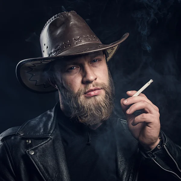 Smoking man with a beard and mustache wearing a cowboy hat. — Stock Photo, Image