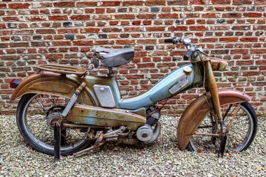 1960 'lardan kalma klasik bir motosiklet, renkli giyilmiş, küçük taşlı sokak, arka planda tuğla duvar, eski, kırık, paslı ve eski moda vitrin.