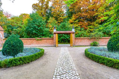 Kapıya giden kaldırım taşı yolu kiremit duvarlar arasında kiremit çatılı, bir malikanenin ön bahçesi, çalılarla çevrili küçük yeşil ağaçlı ekici, bol sonbahar yapraklı, Belçika 'da bulutlu bir gün.