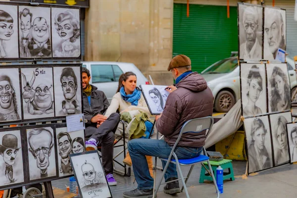 Barselona, İspanya. 9 Şubat 2014. Bir ressam, kömür ya da tebeşirle sandalyeye oturmuş turistlere satmak için sokakta kömür portreleri yapan bir çift çiziyor. Şehir sanatı konsepti