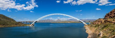 Roosevelt Lake Bridge Panorama. Panoramic view of Bridge in Arizona Sonoran Desert in a beautiful sunny day with a blue sky and fluffy white clouds. Deep blue water reservoir on tSalt River of Tonto National Forest. clipart