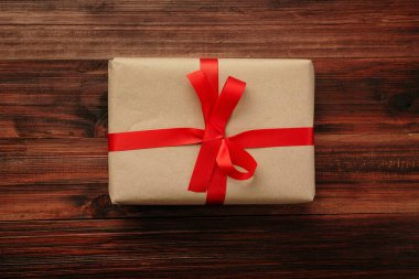 Yılbaşı ve yeni yıl hediyesi paketli Kraft kahverengi kağıt ve ahşap masa arkaplan manzaralı kırmızı kurdele.
