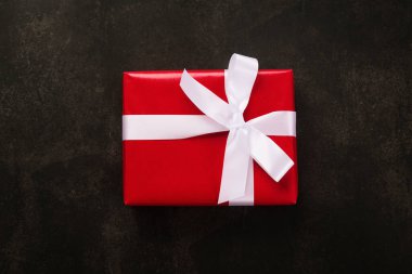 Kırmızı kağıt ve beyaz kurdeleyle sarılı Noel hediyesi kutusunun üst görünümü grunge arkaplanda.