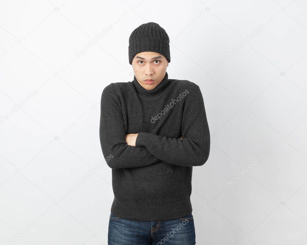 Young handsome asian man wearing grey sweater and beanie hugging herself and trembling, shaking from cold wind, freezing on white background.