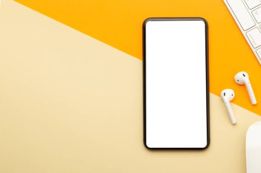 Düz yatış, turuncu ofis masasının üst görüntüsü akıllı telefon boş ekran maketi kırpma yolu, kablosuz kulaklıklar, klavye, fare. Modern çalışma alanı.