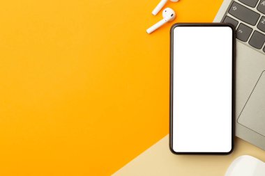 Düz yatış, turuncu ofis masasının üst görüntüsü akıllı telefon boş ekran maketi kırpma yolu, kablosuz kulaklıklar, bilgisayar. Modern çalışma alanı.