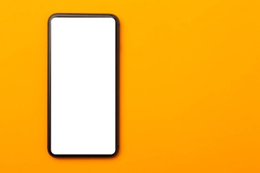 Düz yerde, turuncu ofis masasının üst görüntüsü. Akıllı telefon boş ekran maketi ve kırpma yolu. Modern çalışma alanı.