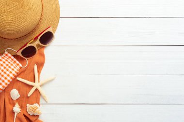Plaj aksesuarlarıyla yaz arkaplanı - hasır şapka, güneş gözlüğü, havlu ve maske beyaz ahşap masa arkaplan görünümlü covid-19 önlemek için fotokopi alanı ile.
