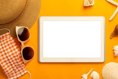 Boş ekran tablet bilgisayar ve plaj aksesuarları ile yaz arkaplanı, canlı turuncu arkaplan görünümlü covid-19 önleme maskesi kopyalama alanı ile.