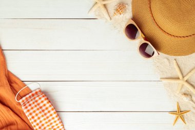 Plaj aksesuarlarıyla yaz arkaplanı - hasır şapka, güneş gözlüğü, havlu ve maske beyaz ahşap masa arkaplan görünümlü covid-19 önlemek için fotokopi alanı ile.
