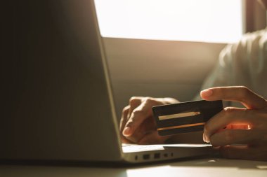 Erkek eller kredi kartını tutuyor ve işten, e-ticaretten, internet bankacılığından ayrılırken online alışveriş için çalışma masasında dizüstü bilgisayar kullanıyor..