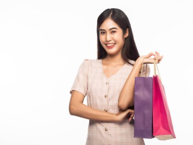 Gülümseyen güzel Asyalı kadın portresi elbise giyiyor ve beyaz arka planda izole edilmiş alışveriş torbaları tutuyor..