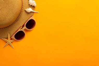 Plaj aksesuarlarıyla yaz arkaplanı - hasır şapka, parlak turuncu arka plan manzaralı güneş gözlüğü.