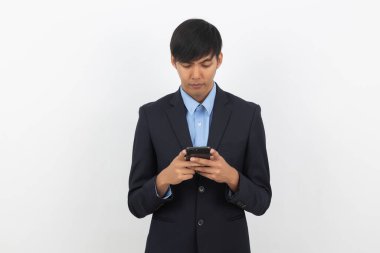 Genç Asyalı yakışıklı iş adamı, beyaz arka planda şüpheli görünen akıllı telefon kullanıyor..