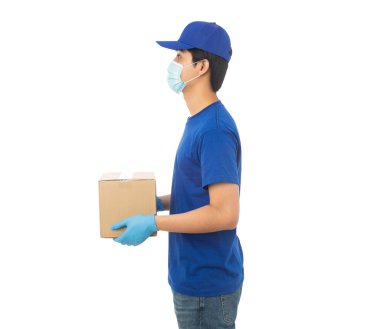 Maske takan ve eldiven takan genç teslimatçı elinde karton kutu ile beyaz arka planda izole edilmiş kırpma yolu ile izole edilmiş karton kutu tutuyor..