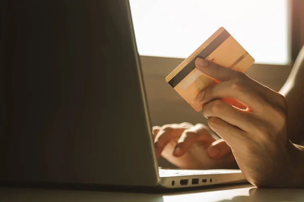 Male hands holding credit card and using laptop computer at working desk for online shopping while break from work at home, E-commerce, Internet banking.