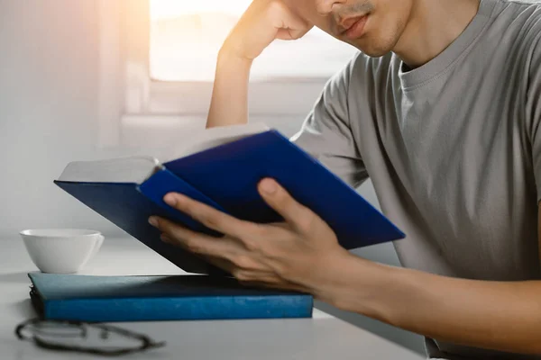 Young man reading book at work desk in free time from working at home, Knowledge and learning concept.