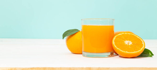 Fresh orange juice in glass and oranges fruit on white wooden table with blue banner background with copy space.