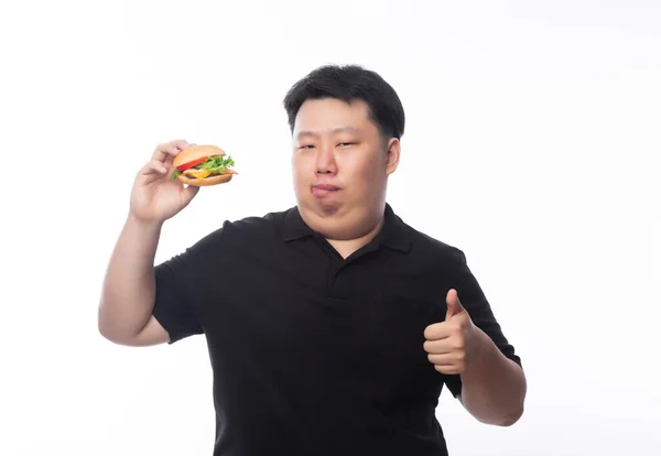 若い面白い脂肪アジアの男を保持ハンバーガーと表示親指アップ白い背景に隔離されました 不健康な概念 — ストック写真