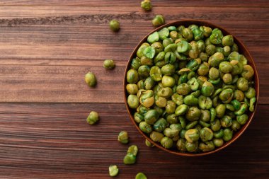 Masadaki ahşap kasedeki tuzlu yeşil bezelye, düz uzanmış, sağlıklı atıştırmalık, vejetaryen yemeği..