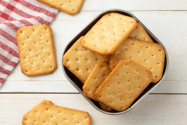 Beyaz ahşap masa arkasında masa örtüsü olan paslanmaz çelik bir kasede kraker kurabiyeleri..