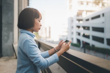 Caddenin karşısında cep telefonu kullanan Asyalı genç bir kadın..