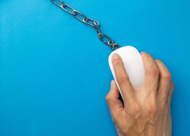 Masaya zincirlenmiş bir bilgisayar faresinin üst görüntüsü. İnternet bağımlılığı için kavramsal imaj, uzaktan çalışma tükenmesi, dijital kölelik, ofis stresi ve sağlıklı dijital detoks ihtiyacı..