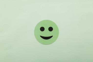 Açık yeşil arka planda gülen bir yüzü olan yeşil kağıt çemberi. Mutluluk, akıl sağlığı, müşteri memnuniyeti ve pozitiflik için kavramsal imaj. Kopyalama alanı olan minimalist biçim.