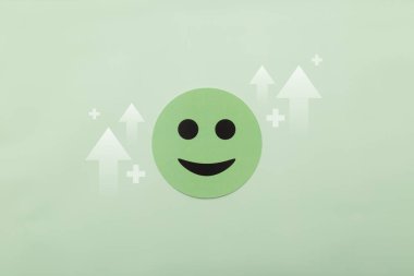 Yükselen okları ve yeşil arka planda artı işaretleri olan yeşil gülen surat. Büyüme, zihinsel sağlık gelişimi, artan memnuniyet ve olumlu iş sonuçları kavramı. Minimalist düzlük.