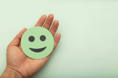 Yumuşak bir zeminde yükselen okları olan yeşil gülen yüzlü bir kağıt tutuyordu. Zihinsel sağlık iyileştirmesi, pozitif iş büyümesi, müşteri memnuniyeti ve duygusal refah kavramı.