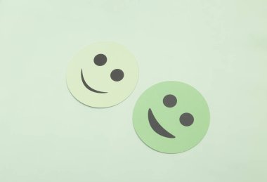 Pastel arka planda fotokopi alanı olan iki yeşil kağıt kesiği, gülen surat. Zihinsel sağlık konsepti, olumlu geri bildirim, müşteri memnuniyeti ve temiz minimalist tarzda mutluluk..